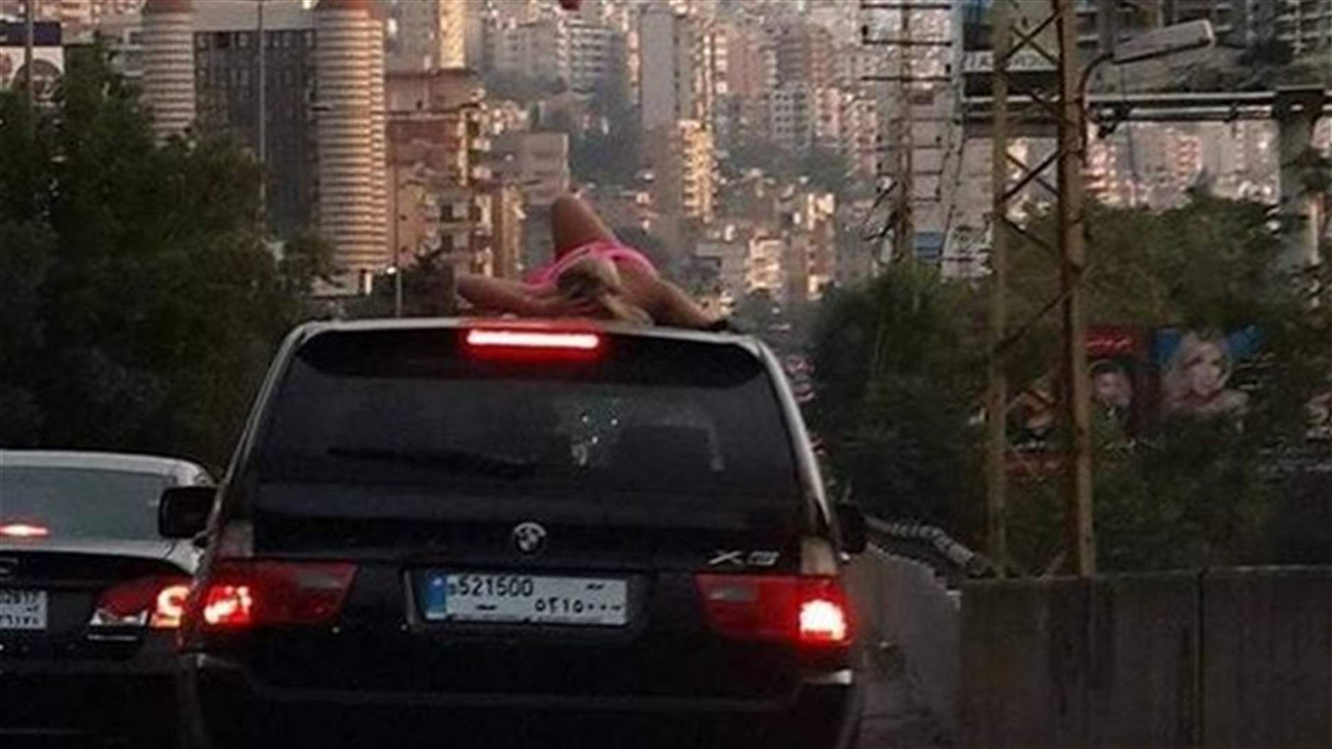 شابة بالمايوه "تتشمّس" على سطح سيارة وسط زحمة السير